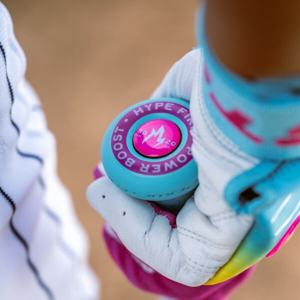 A close-up shows a gloved hand gripping the blue Power Boost grip of the 2026 Easton Hype Fire (-5) USSSA Baseball Bat (EUT6HYP5); the gloves are white, pink, and blue with flames, and part of a striped uniform is visible.