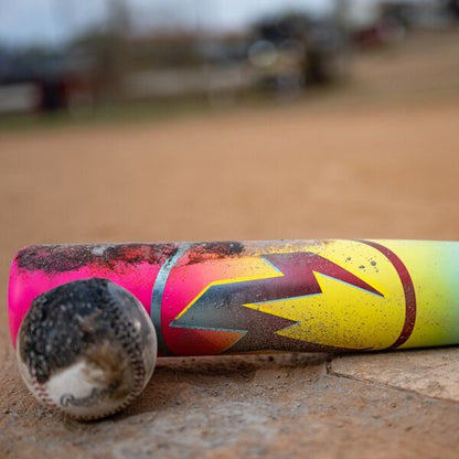 A close-up of a worn baseball and a dirt-stained 2026 Easton Hype Fire (-5) 2 3/4" USSSA Baseball Bat (EUT6HYP5) with ThermoComposite technology and a bold multicolored pattern, lying on a dusty field.