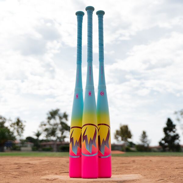 Three vibrant baseball bats, including the 2026 Easton Hype Fire (-5) USSSA Baseball Bat by Easton, stand upright on a field with blue handles and pink-yellow gradient barrels, set against a backdrop of clouds and trees.