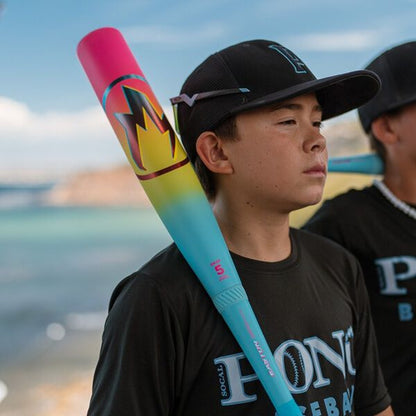 A boy in a black baseball cap and shirt holds the 2026 Easton Hype Fire (-5) 2 3/4" USSSA Baseball Bat (EUT6HYP5) over his shoulder, standing outdoors near water with another player visible in the background.