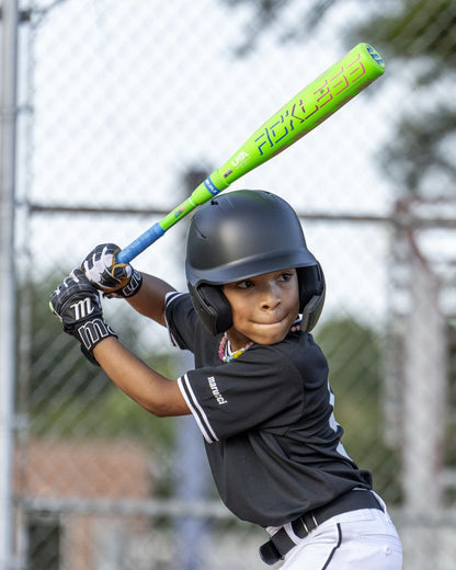 A young baseball player wearing a black helmet and uniform prepares to swing the Marucci 2027 RCKLESS Gen 2 Composite (-10) 2 5/8″ USA Baseball Bat (MSBRC210U) with maximum barrel flex during a game, standing ready at home plate with a focused expression.