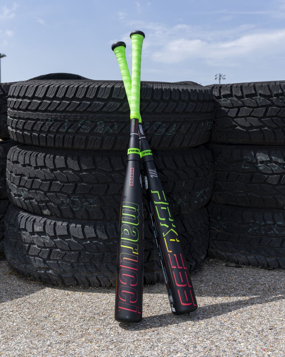 Two Marucci 2027 RCKLESS Gen 2 Composite (-5) USSSA baseball bats with neon green handles, maximum barrel flex, and vibrant branding rest together against a stack of large black tires outdoors on a sunny day.