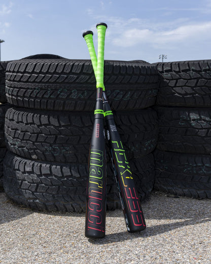 Two Marucci 2027 RCKLESS Gen 2 Composite (-5) USSSA baseball bats with neon green handles, maximum barrel flex, and vibrant branding rest together against a stack of large black tires outdoors on a sunny day.