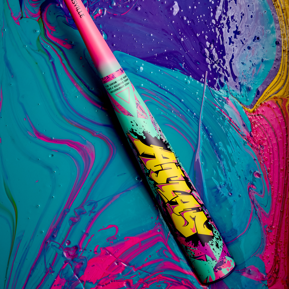 The 2026 Louisville Slugger Atlas Wildstyle (-3) BBCOR Baseball Bat: WBL4178010 rests diagonally on a striking background of swirling blue, pink, purple, and yellow, showcasing bold pink, yellow, teal, and black designs on its 1-piece alloy construction.