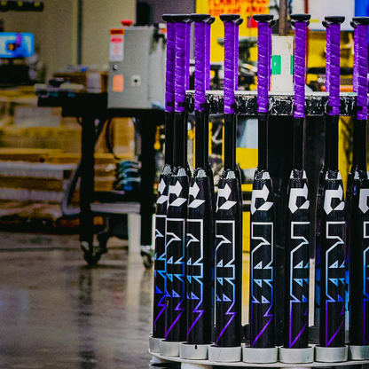 A lineup of black and purple 2026 DeMarini Prism+ (-11) Fastpitch Softball Bats (WBD2636010) stands upright in a factory, displaying the FURY graphic and innovative Continuous Fiber Composite Barrel design by DeMarini.