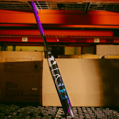 A 2026 DeMarini Prism+ (-11) Fastpitch Softball Bat (WBD2636010) leans against a shelf in a warehouse, surrounded by cardboard boxes and metal racks.