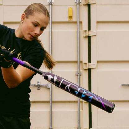 A young girl in a black shirt and gloves readies to swing a 2026 DeMarini Prism+ (-11) Fastpitch Softball Bat (WBD2636010), with a beige metal door featuring vertical lines in the background.