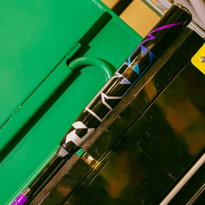 A 2026 DeMarini Prism+ (-11) Fastpitch Softball Bat (WBD2636010) with blue and purple geometric designs rests diagonally on a shiny black and yellow metal surface, with a green locker in the background.