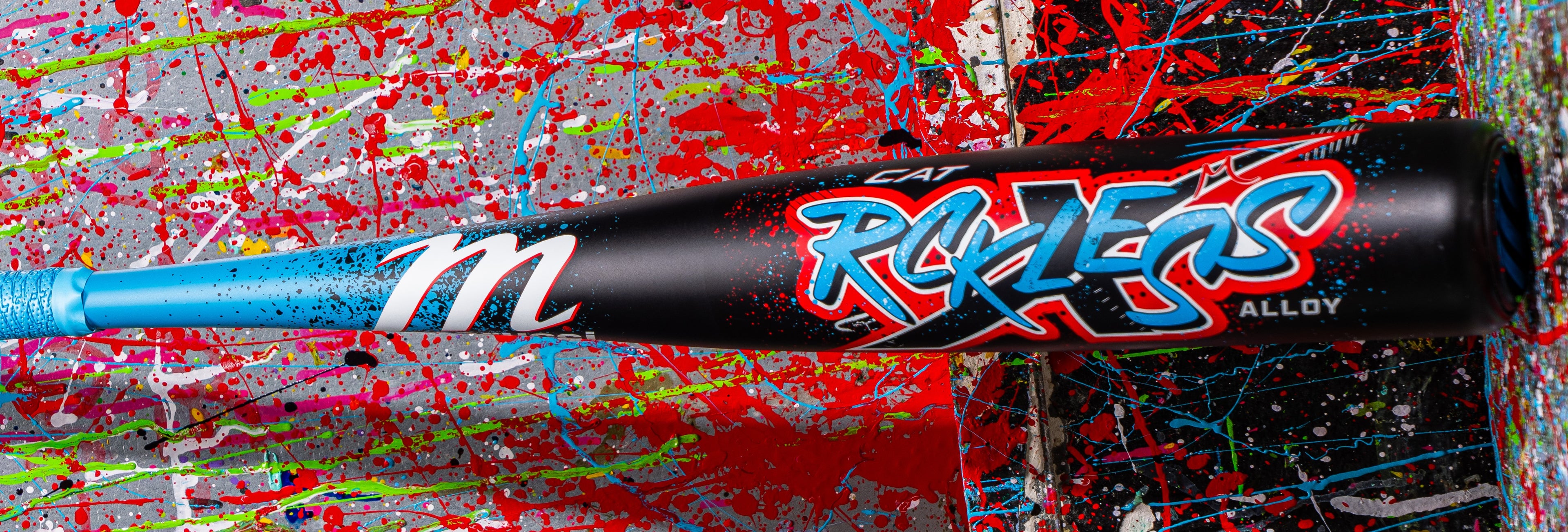 A colorful baseball bat with “CAT RX XEGA ALLOY” and a stylized “m” logo, lying against a splattered, paint-covered background in red, blue, green, and pink.