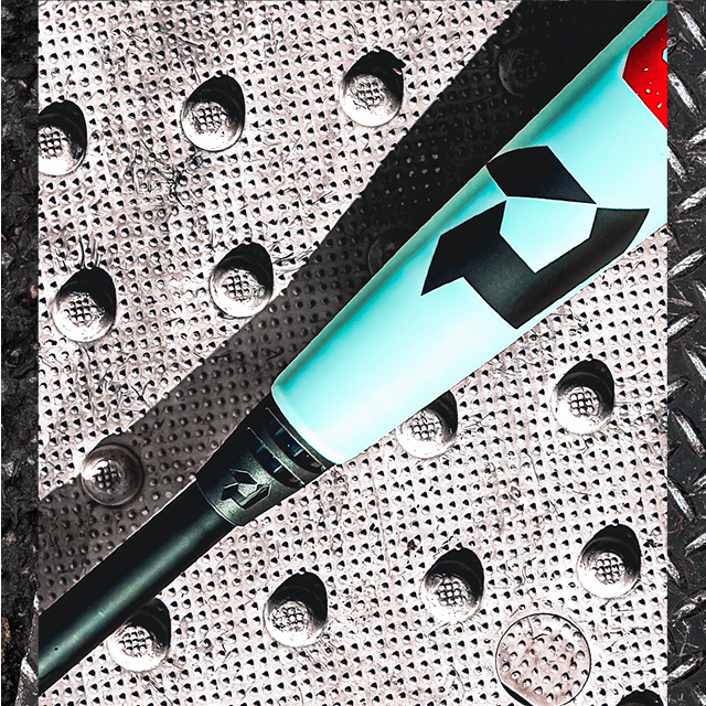 A close-up of a light blue baseball bat with a black geometric logo lying diagonally on a textured metal surface with raised circular bumps.