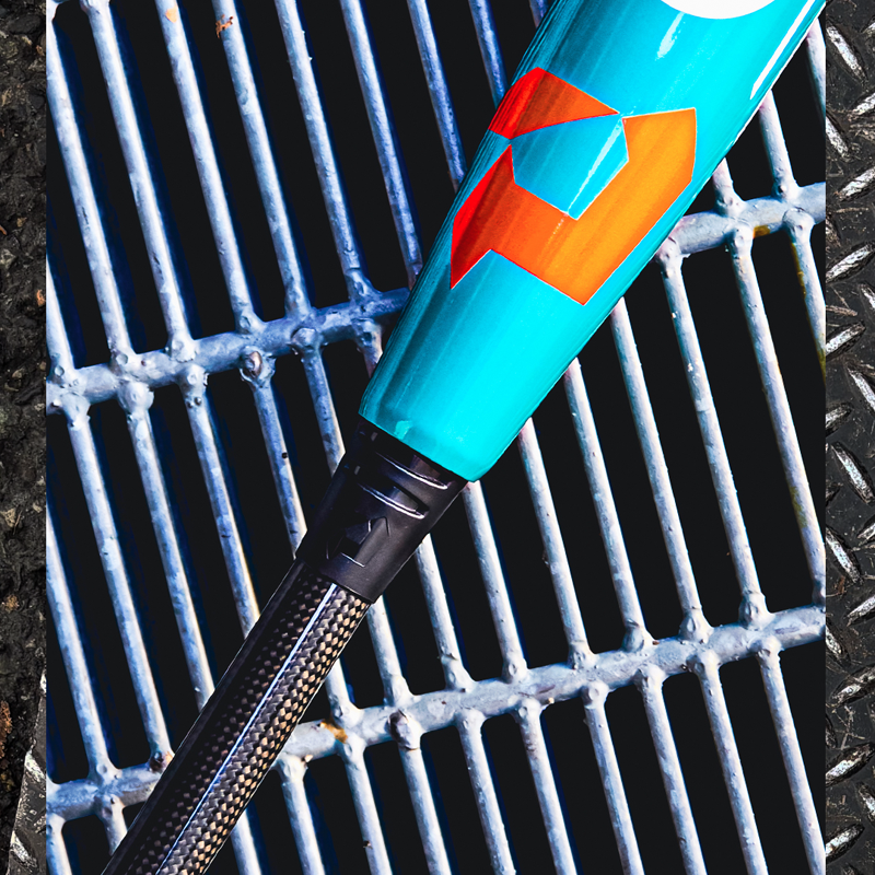 A close-up of a teal and orange baseball bat with a black handle resting on a metal grate beside a textured metal surface.