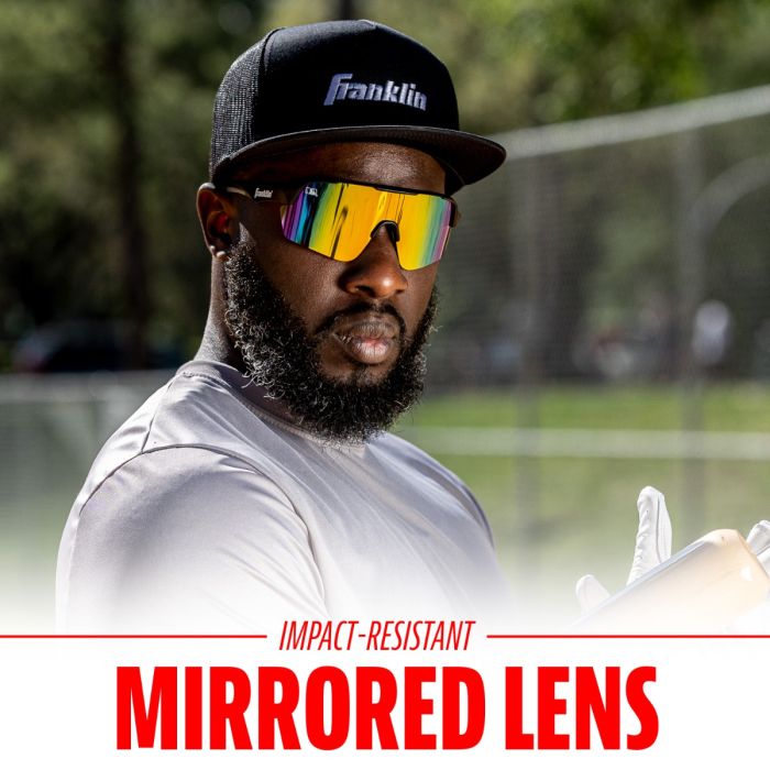 A bearded man in a black cap, white shirt, and Franklin MLB Pro Sunglasses: 24012C stands outdoors holding a baseball glove. The text below reads: Impact-Resistant Mirrored Lens by Franklin.