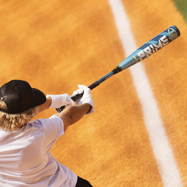 A player wearing a black cap and white gloves swings the 2025 Louisville Slugger Meta Prime (-8) USSSA Baseball Bat (WBL2971010) near the foul line on a dirt field.