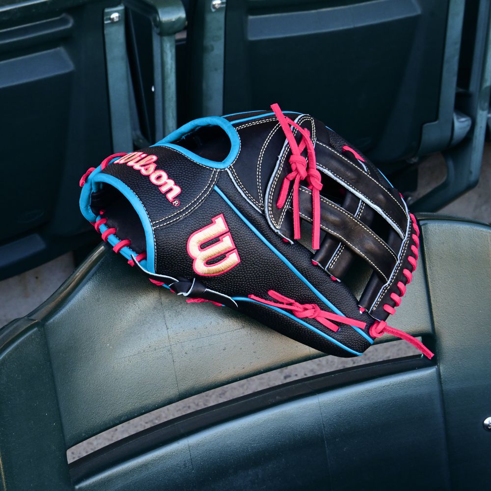 A Wilson A2000 1777SS 12.75" Baseball Glove (WBW1032221275) in black with SuperSkin, red and blue laces rests on a green stadium seat, empty seats in the background.