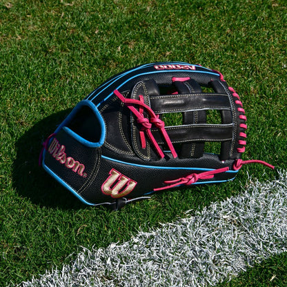 A Wilson A2000 1777SS 12.75" Baseball Glove (WBW1032221275), black with SuperSkin, blue trim, and pink laces, rests on green grass near a white chalk line on a sports field.