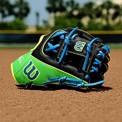 A Wilson A2000 PF88SS 11.25" Baseball Glove (FALL 2025) in black, green, and yellow with blue laces lies on a baseball field’s dirt infield; blurred trees and a fence are visible in the background.