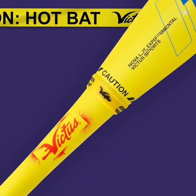 A bright yellow baseball bat labeled Victus with CAUTION: HOT BAT tape wrapped around it, set against a purple background. The bat also features CAUTION and product details near the handle.