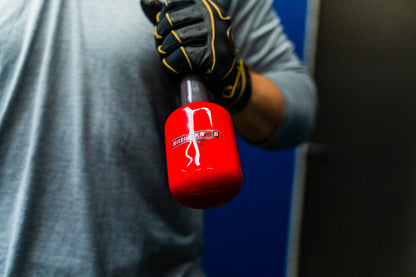 A person in a gray shirt and black gloves holds The Hitting Knob Bat Weight by Hitting Knob—a bright red baseball training aid to increase bat speed—against a blue and black background.