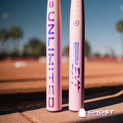 Two pink 2026 Easton Ghost Unlimited (-10) Fastpitch Softball Bats (EFP6GHUL10) with bold purple UNLIMITED and Double Barrel EXT text stand upright on a dirt field, with blurred palm trees and a Ghost Unlimited logo nearby.
