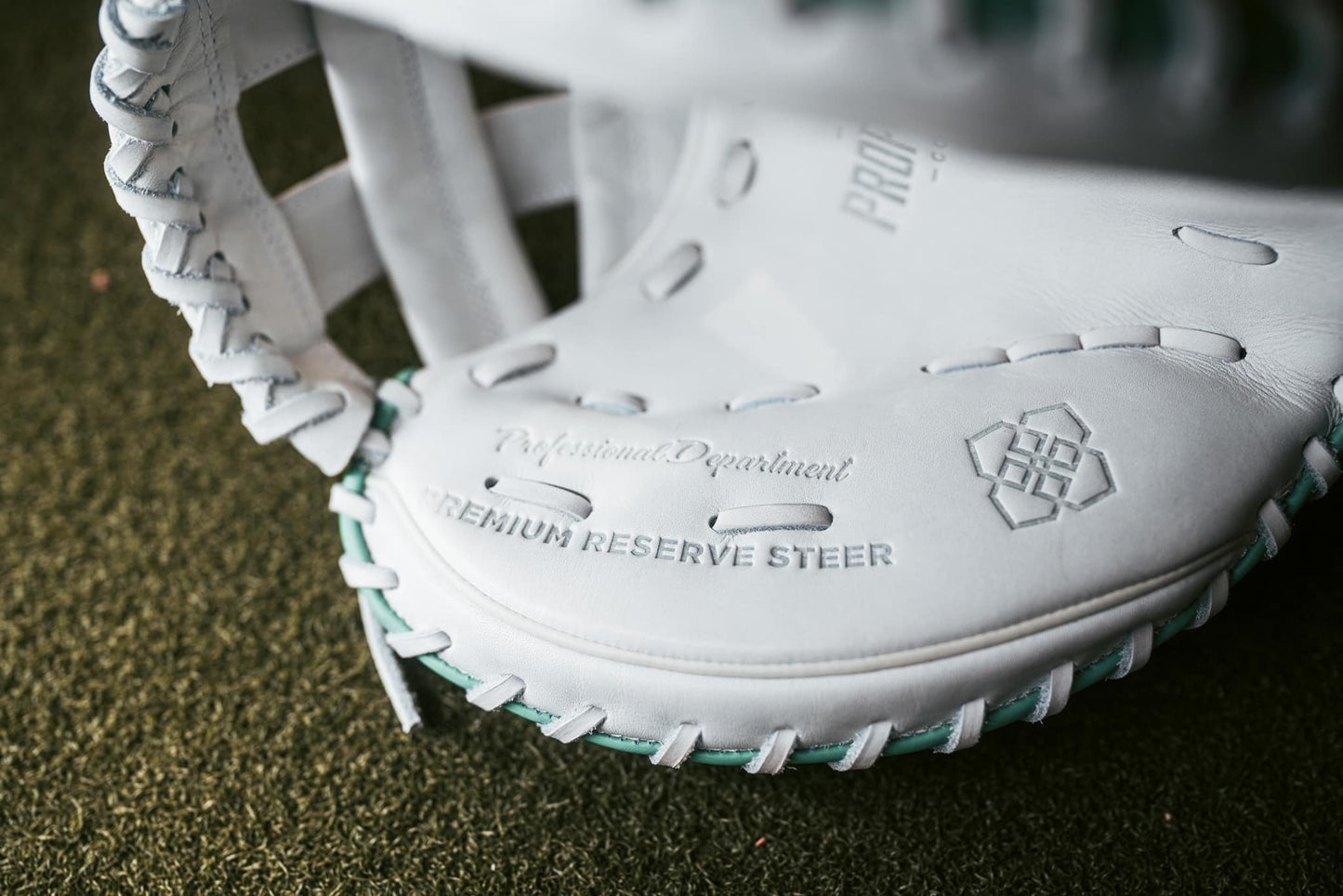 A close-up of the Easton Jen Schro "The Rudi" 34" Fastpitch Catcher's Mitt (RUDI-2024), featuring green laces and embossed with "Professional Department" and "Premium Reserve Steer," rests on green artificial turf.