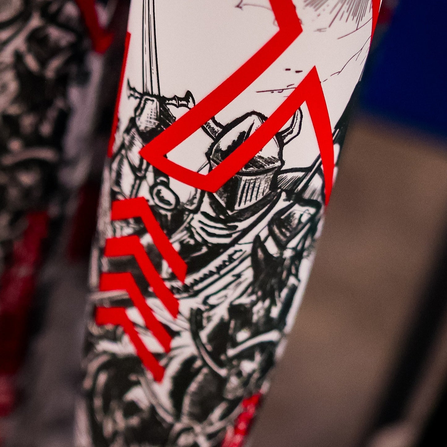 Close-up of a surface with intricate black and white medieval knight designs and bold red geometric lines—reflecting the dynamic style of the DeMarini 2026 Exile (-3) BBCOR Baseball Bat: WBD2589010.