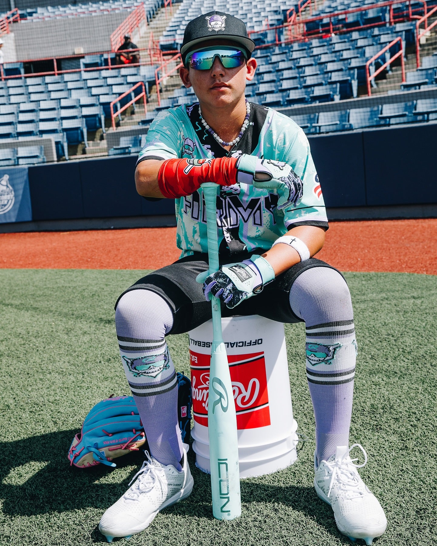 A man sits on a white bucket holding a 2026 Rawlings Icon (-5) 2 3/4" USSSA Baseball Bat (RUT6I5) by Rawlings.