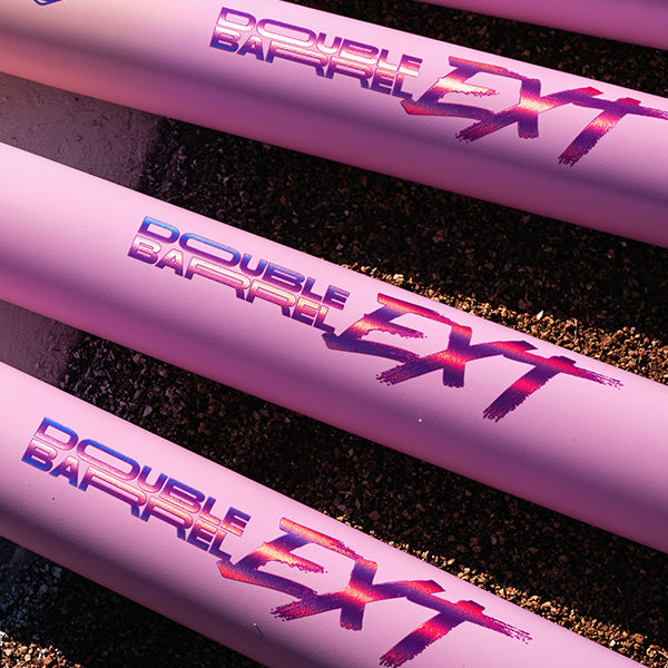 A close-up of several 2026 Easton Ghost Unlimited (-10) Fastpitch Softball Bats (EFP6GHUL10) by Easton, featuring bold Double Barrel EXT graphics in purple and pink, lying side by side on a rough surface.
