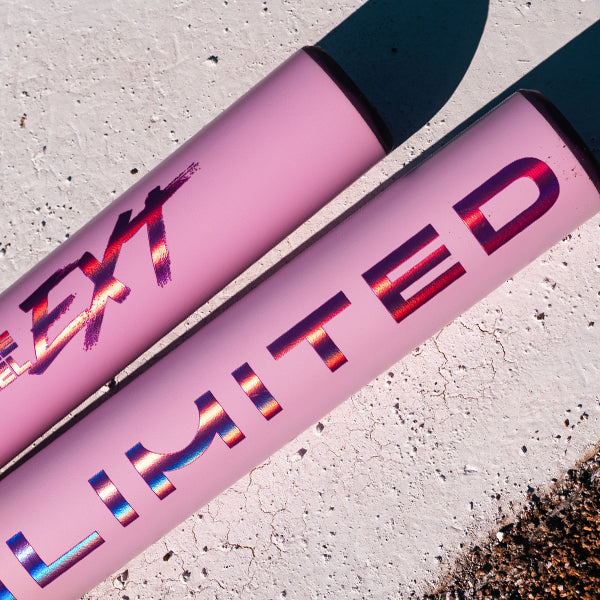 Two pink cylindrical items rest side by side on a textured white surface. One reads LIMITED in shiny, gradient text; the other, an Easton 2026 Ghost Unlimited (-10) Fastpitch Softball Bat, shows partially visible distressed EXT lettering.