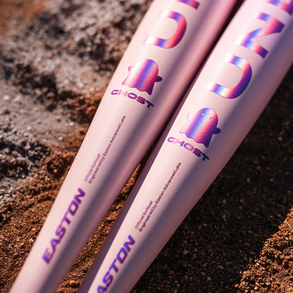 Two 2026 Easton Ghost Unlimited (-10) Fastpitch Softball Bats by Easton, featuring purple lettering and ghost graphics, lie side by side on reddish-brown dirt.