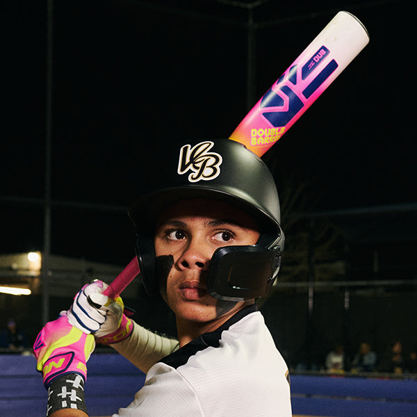 A young player in a black helmet and pink gloves grips an Easton 2026 Dub (-10) 2 3/4" USSSA Baseball Bat (EUT6DUB10) with two-piece composite construction, preparing to swing under stadium lights.