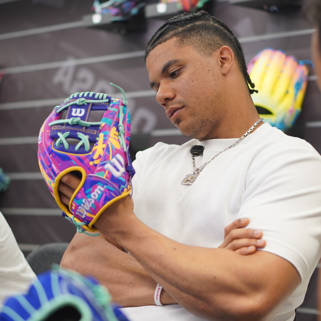 A man in a white shirt examines the Wilson A2000 1786SS 11.5" Baseball Glove (GOTM January 2026) with vibrant colors and Pro Stock leather, standing before a display wall of other colorful Wilson gloves.