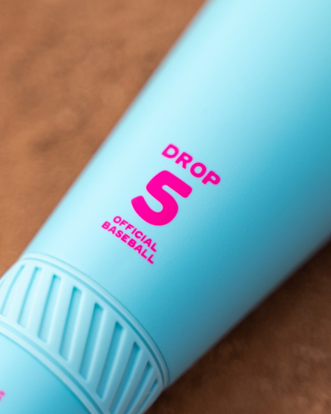 A close-up of a blue cylinder labeled DROP 5 OFFICIAL BASEBALL in pink, set against a brown background, evoking the 2026 Easton Hype Fire (-5) 2 3/4" USSSA Baseball Bat: EUT6HYP5 by Easton.