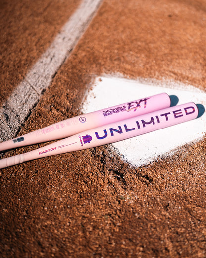 Two pink Easton Ghost Unlimited (-8) Fastpitch Softball bats (model EFP6GHUL8) lie on a dirt baseball field next to home plate.