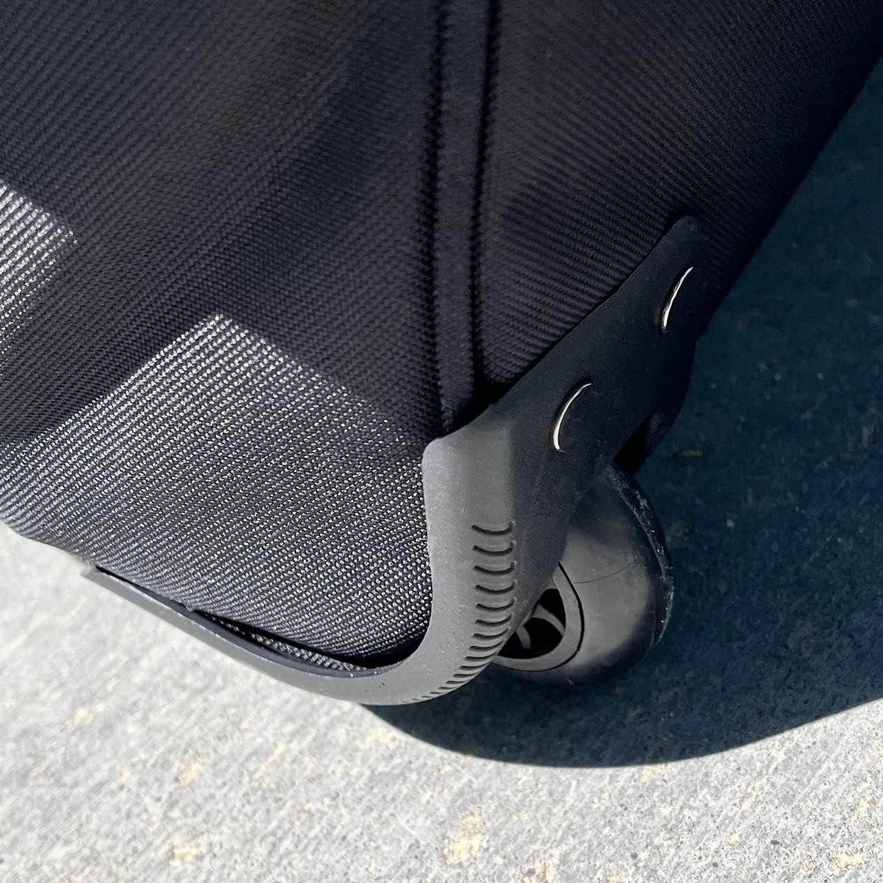 Close-up of the Champro Boss Wheeled Catcher's Bag: E92 by Champro Sports, showing its black rugged all-terrain wheel and corner protector, resting on a textured gray surface in bright sunlight.