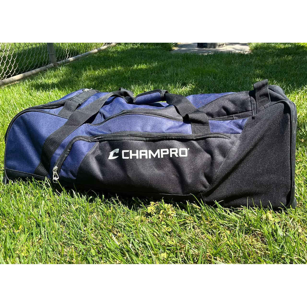 The Champro Sports Boss Wheeled Catcher's Bag: E92, featuring a spacious bat pocket, rests on the grass ready for action.