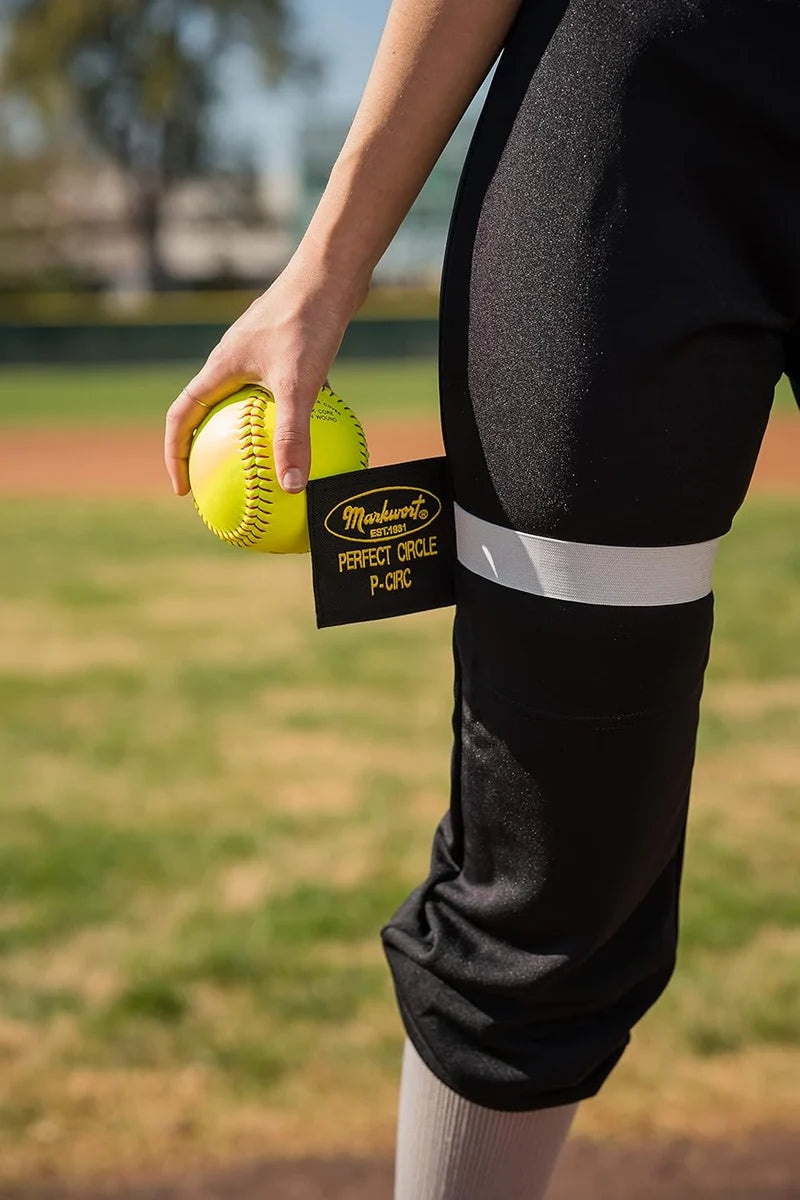 A softball player holding a yellow softball, with a Markwort The Perfect Circle Pitcher’s Training Aid: PCIRC wrapped around her thigh as a pitching aid.