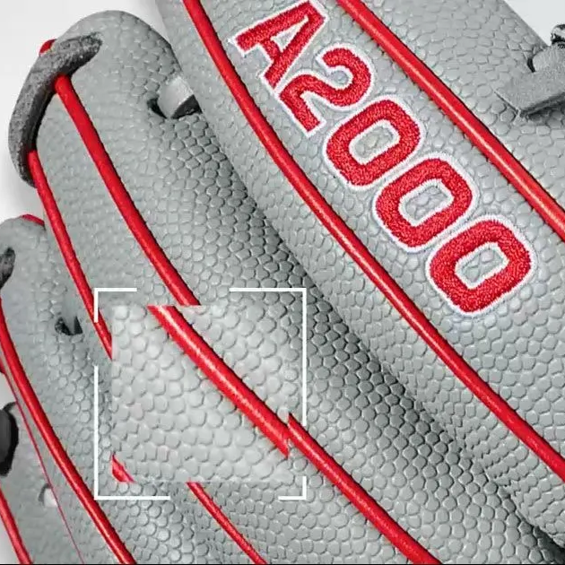 Close-up of a grey textured baseball glove with red stitching and the label A2000 embroidered in red.