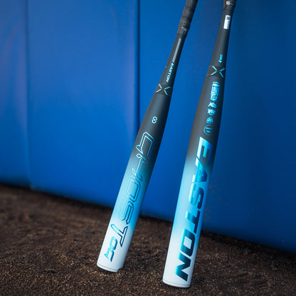 Two Easton Ghost OG (-11) 2025 Fastpitch Softball Bats by Easton stand upright against a blue padded wall on a dirt surface.