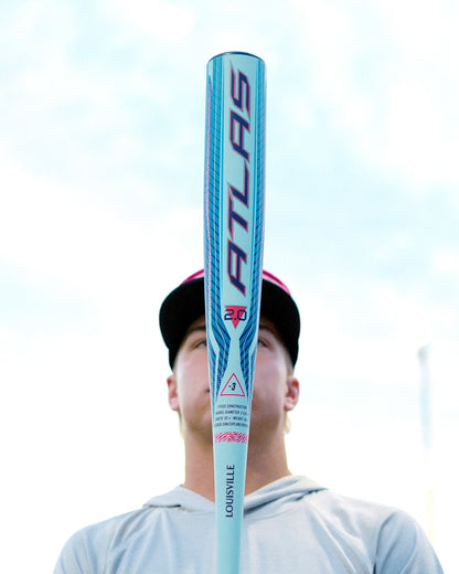 A person stands facing the camera, mostly hidden behind a blue and pink 2027 Louisville Slugger Atlas 2.0 (-3) BBCOR Baseball Bat (WBL4248010) held upright in front of their face against a bright sky background.