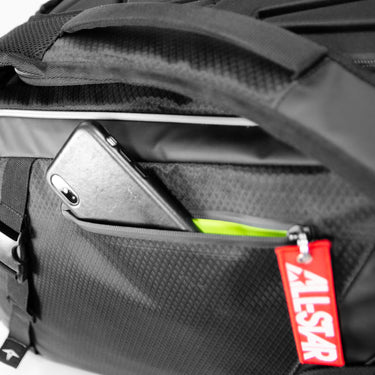 A close-up of the All Star MVP PRO Series Catcher's Backpack: BBCBP shows a zippered pocket partially open with a smartphone and neon green item inside, plus a red ALSAR keychain attached to the zipper pull.