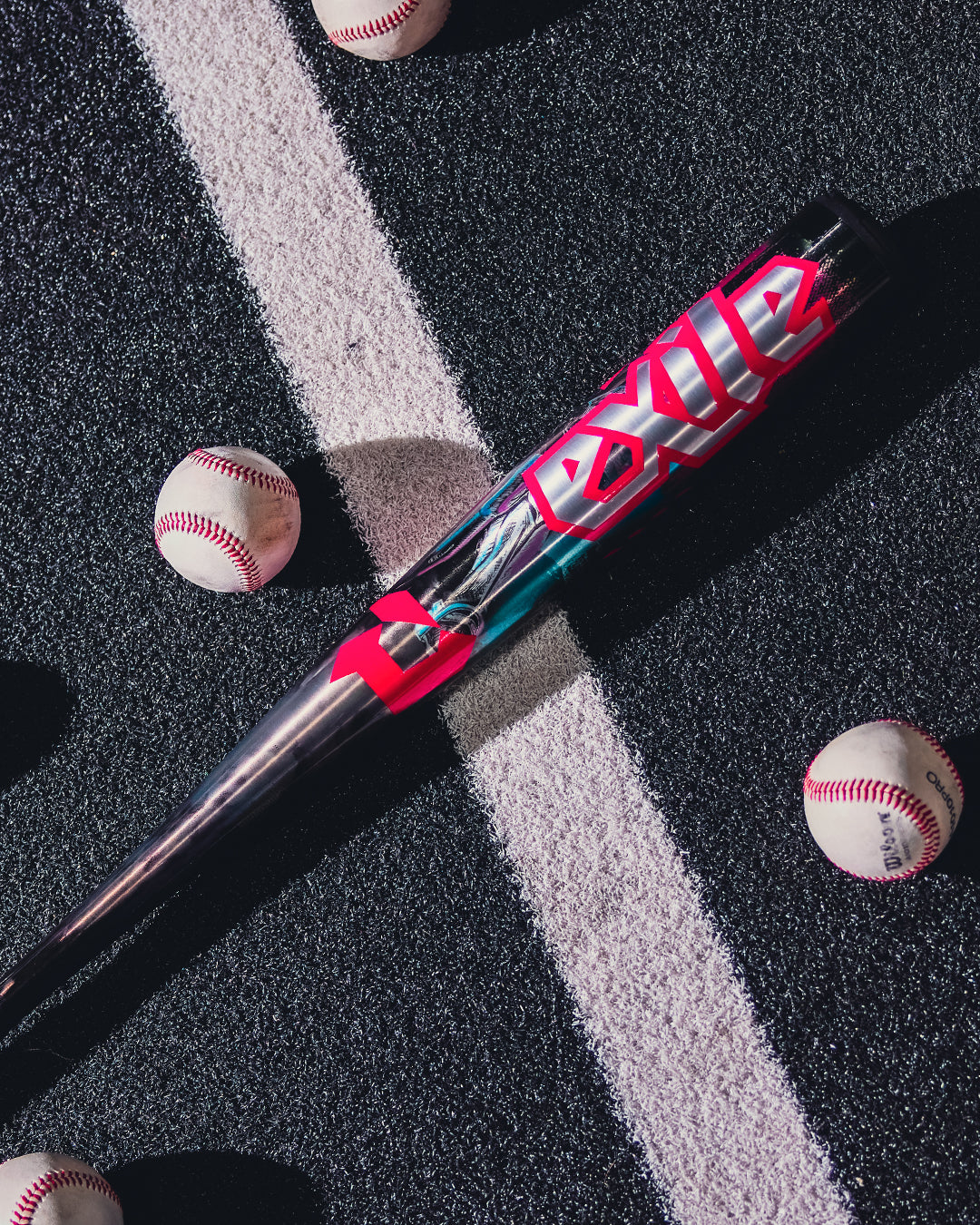 A 2026 DeMarini Exile Cyborg (-3) BBCOR Baseball Bat (WBD2654010) with bold red and white EXILE text lies on a striped blacktop, surrounded by four baseballs.