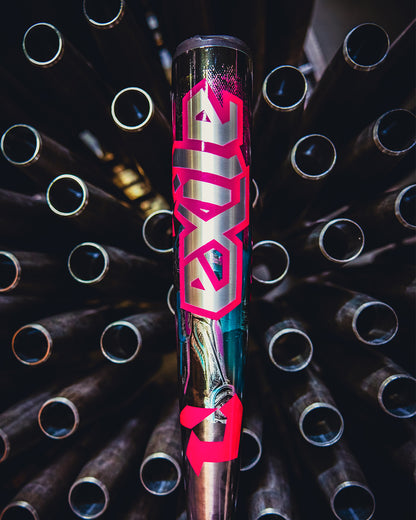 A close-up of the 2026 DeMarini Exile Cyborg (-3) BBCOR Baseball Bat (WBD2654010), featuring bold pink "Exile" lettering and standing upright among stacked metal pipes in the background.