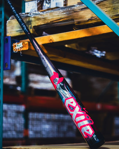 A black and red 2026 DeMarini Exile Cyborg (-3) BBCOR Baseball Bat (WBD2654010) with bold lettering leans against a metal rack in an industrial warehouse.