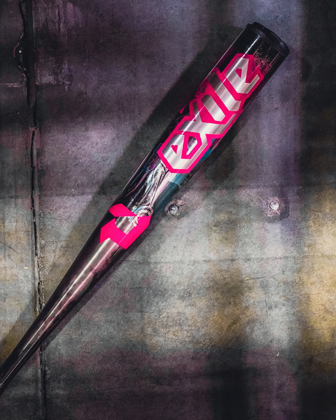 The 2026 DeMarini Exile Cyborg (-3) BBCOR Baseball Bat (WBD2654010) rests diagonally on worn concrete, featuring metallic design, bold pink Exile lettering, and an X14 Alloy Barrel for serious players.
