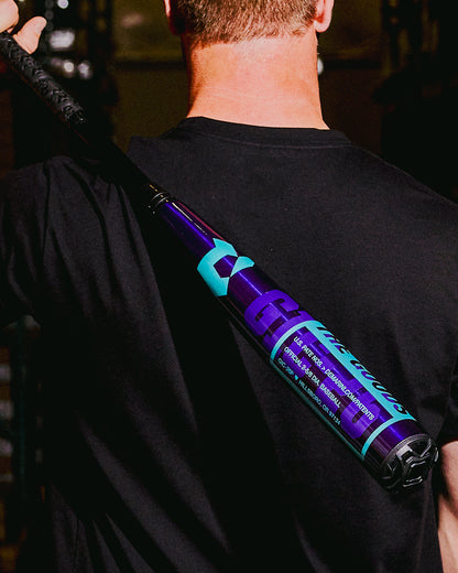 A person in a black shirt holds a Royal Purple 2026 DeMarini The Goods (-3) BBCOR Baseball Bat (model WBD2634010) over their shoulder, with the DeMarini branding and text clearly visible.