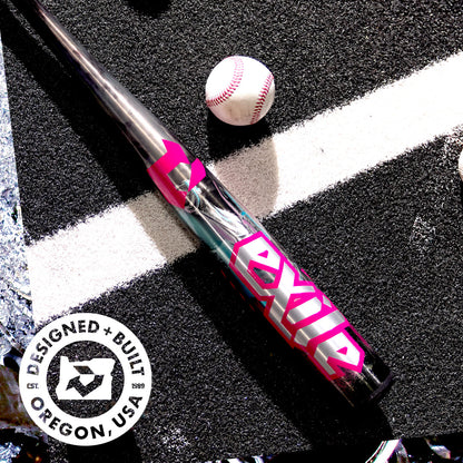 A metallic DeMarini 2026 Exile Cyborg (-3) BBCOR Baseball Bat (WBD2654010), with bold pink and white EXILE letters, lies on asphalt by a white baseball. A circular logo reads DESIGNED + BUILT OREGON, USA in the bottom left corner.