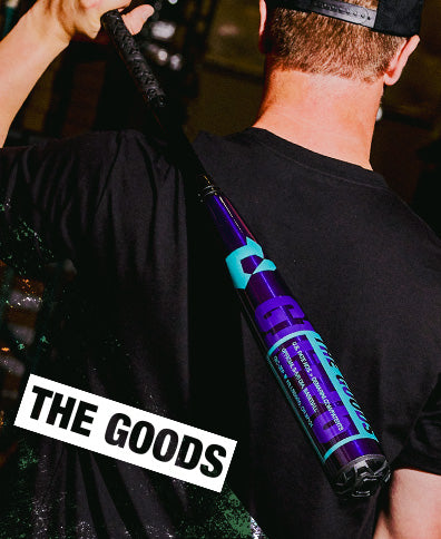 A person in a black shirt and cap holds the 2026 DeMarini The Goods Royal Purple (-3) BBCOR Baseball Bat (WBD2634010) over their shoulder. "THE GOODS" is displayed in bold white letters at the bottom left corner.