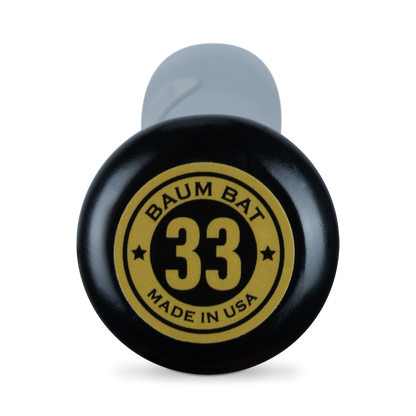 Close-up of the knob of a black Baum Gold Stock AAA Pro Balanced Composite Wood Bat: BBM, featuring a yellow and black circular label reading BAUM BAT 33 MADE IN USA with two stars. The partially visible handle is wrapped in a gray grip—engineered with advanced composite wood bat technology for elite performance and proudly handcrafted in the USA by Baum.