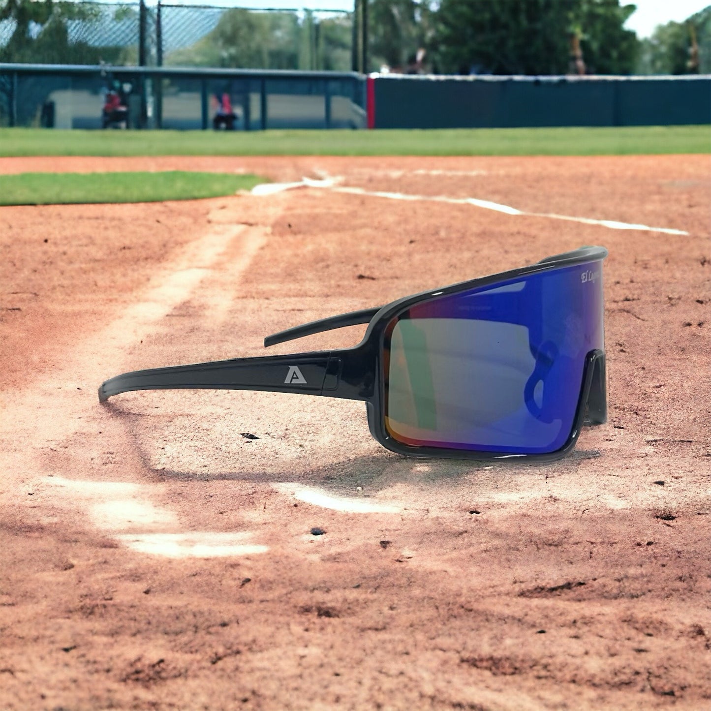 A pair of Akadema El Legendo Sunglasses (ELLEGENDO) with UV400 protection rests on home plate of a baseball field, surrounded by green grass and a fence in the background.