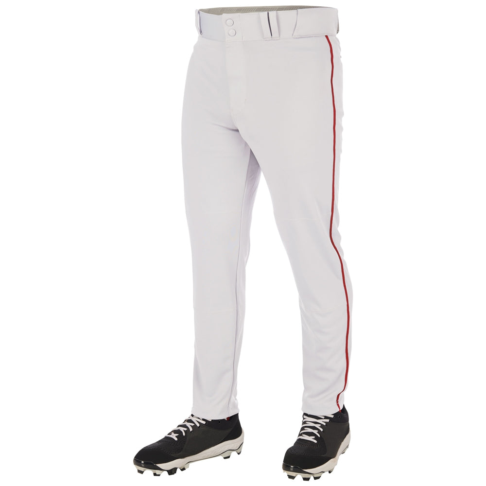 The image shows a person wearing Champro Sports Triple Crown 2.0 Tapered Baseball Pants with red piping (BP66), made from pro-weight fabric, paired with black cleats with white laces; the photo is cropped from the waist down.